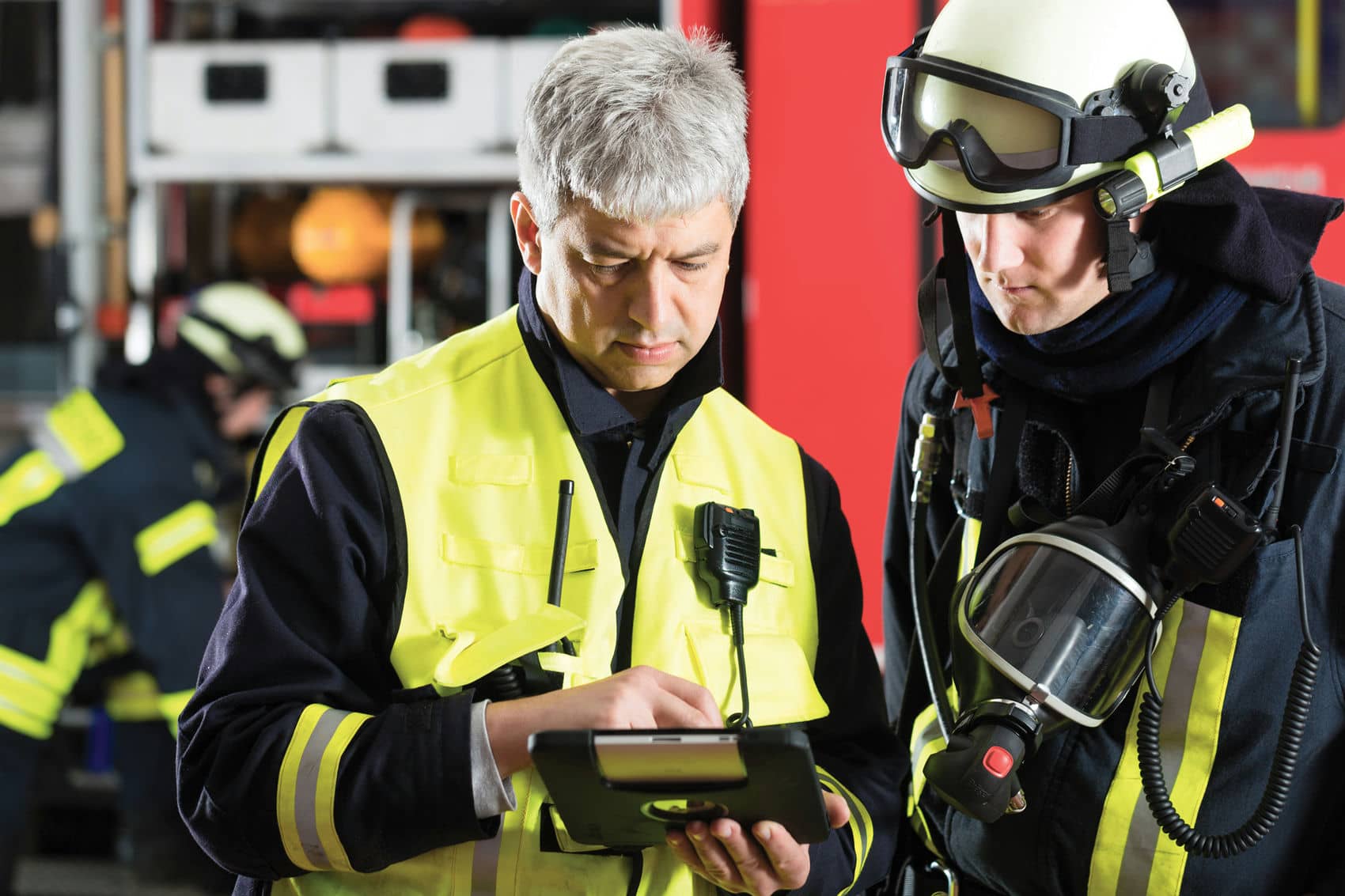 Two firefighters in safety gear looking at a tablet